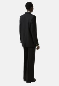 Black tailored suit with long jacket and wide-leg trousers, featuring a patterned lining on the cuffs and smooth fabric texture.