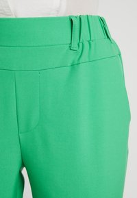 Groene, hoge taille broeken van een soepele, textuurstof. Voorzien van een subtiele zak en een tailleriem met lussen.
