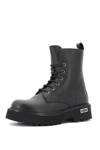 Bota de tobillo de cuero negro con cordones en el frente, ojales plateados y una suela negra gruesa. Presenta un acento de logo en el lateral y un acabado suave.