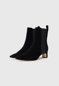 Cizme negre din suede până la gleznă, cu vârf ascuțit, toc mic și pătrat, și panouri laterale elastice. Textură netedă și design minimalist.