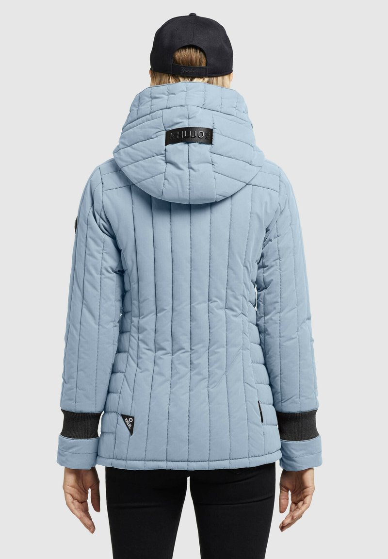 Hellblaue gesteppte Jacke mit Kapuze, ausgestattet mit schwarzen Akzenten und gerippten Bündchen. Sichtbares Logo auf der Rückseite und seitliches Etikett.