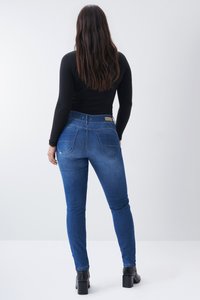 Jeans ajustados azules hechos de mezclilla, con una cintura de altura media, dos bolsillos traseros y detalles de costura sutiles. Combinados con una blusa negra de canalé.
