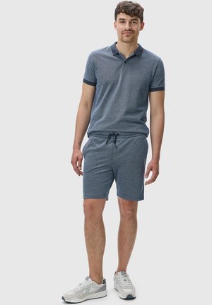 Blå strikket polo med korte ærmer og mørke accenter, parret med matchende shorts med snører, båret med lyse sneakers.