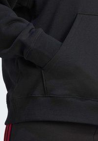 Sweatshirt noir avec poignets et ourlet côtelés, une poche avant, et un tissu doux et texturé. Le design est à coupe ample et minimaliste.