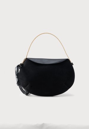 Borsa a mezzaluna in suede nero con patta in pelle, tracolla in pelle regolabile e manico corto a catena dorata su sfondo bianco.