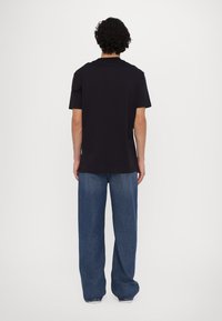 Camiseta de algodón negra con mangas cortas, de corte relajado, que presenta un clásico escote redondo. Llevada con unos jeans de denim azul de corte holgado.