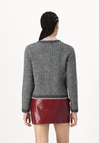 Pelēks adīts džemperis ar faktūru, apaļo izgriezumu un kontrastējošu baltu apdari, kombinēts ar spīdīgu sarkanu ādas mini svārku.