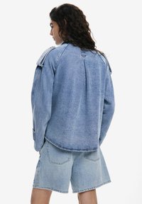 Jachetă din denim de culoare albastră deschisă, cu o croială lejeră, umeri structurați și o pliă pe spate. Asortată cu pantaloni scurți din denim de aceeași culoare.