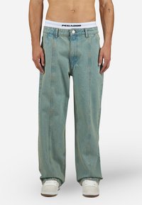 Baggy lyseblå denimbukser med høj talje, featuring en knaplukning, to frontlommer og en hvid taljebånd med "PEGADOR" logo.