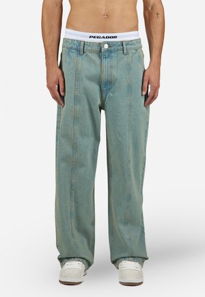 Baggy light blue denim pants with a high waist, featuring a button closure, two front pockets, and white waistband with "PEGADOR" logo.