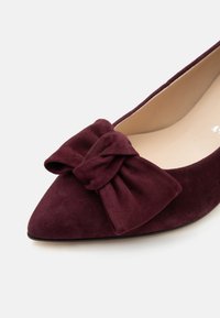 Chaussure plate en daim bordeaux à bout pointu avec un grand nœud en tissu assorti sur la partie avant supérieure.