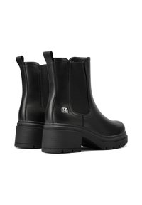 Par de botas de cuero negras hasta el tobillo con tacones gruesos, paneles laterales elásticos, tiradores y un pequeño logo metálico cerca del tacón.