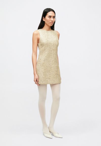 Korte mouwen, knielange jurk van gestructureerde gouden stof. Gecombineerd met doorschijnende witte panty's en witte, puntige platte schoenen. Minimalistisch ontwerp.