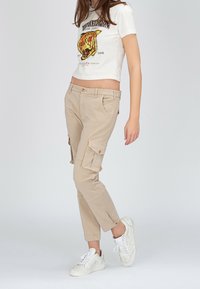 Beiga cargo byxor med flera sidofickor, rak ben-design och knäppning. Kombinerat med en kortärmad vit grafisk t-shirt och vita sneakers.