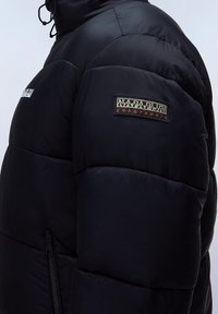 Giubbotto trapuntato nero con una finitura lucida, dotato di tasca frontale con zip e un patch del logo ricamato sulla spalla.