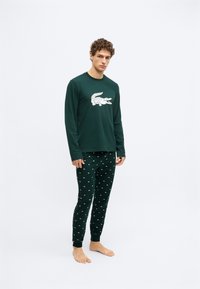 Camiseta de manga larga verde oscuro con gráfico de cocodrilo blanco, combinada con pantalones a juego con pequeños patrones blancos. Tela suave, diseño ajustado.