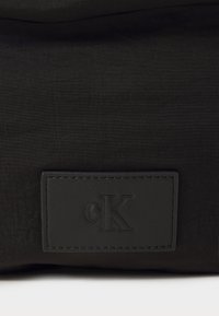 Borsa nera in nylon Calvin Klein con tessuto a trama, toppa con logo in rilievo e dettagli in pelle liscia. Design minimalista senza motivi.