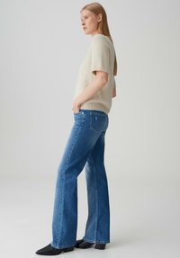 Pull court en maille lâche beige clair à manches courtes assorti à un jean flare taille haute bleu foncé. Des bottines noires à bout pointu complètent le look.