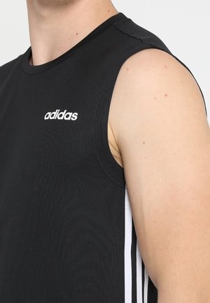 Maillot de sport noir sans manches Adidas avec un logo blanc sur la poitrine et les trois bandes blanches emblématiques sur le côté, porté par une personne.