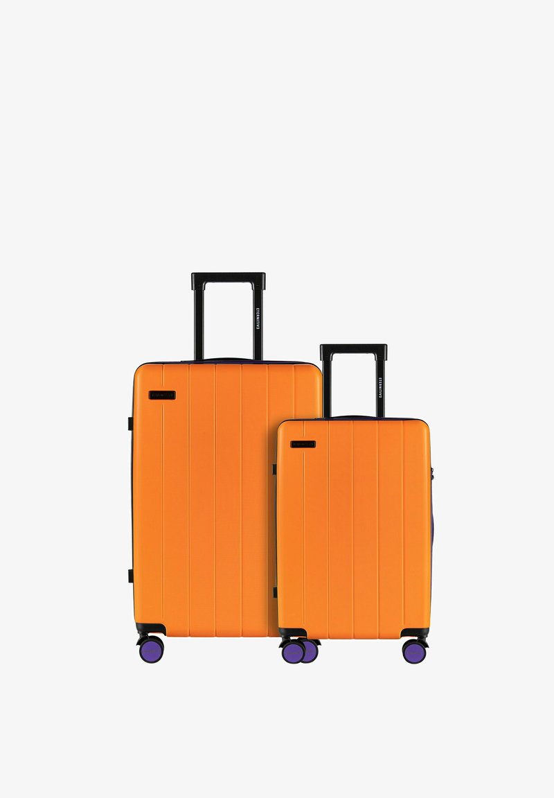 Dwie twarde walizki w jaskrawo pomarańczowym kolorze, ułożone jedna na drugiej. Każda ma czarne uchwyty, teksturowane paski oraz cztery fioletowe kółka zapewniające łatwą mobilność.