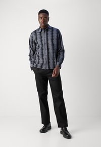 Camisa de manga longa em tecido azul-escuro com um padrão vertical preto; combinada com calças pretas e sapatos pretos brilhantes.