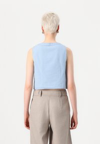 Lichtblauw, mouwloos cropped top van zachte stof, met een ronde halslijn en een eenvoudig ontwerp. Gecombineerd met beige high-waisted broek.