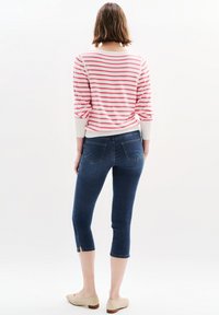 Raitalliset vaaleanpunaiset ja valkoiset pitkähihaiset paita yhdistettynä tummansinisiin nilkkapituisisiin farkkuihin, joissa on sivurei'ät, sekä vaaleat tasapohjaiset kengät.