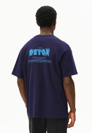 Marineblauw katoenen T-shirt met een grote "DETOX" afbeelding op de achterkant in lichtblauw, met extra tekst in witte letters. Korte mouwen.