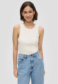 Hellbeige Tanktop mit gerippter Textur, rundem Ausschnitt und dünnen Trägern, kombiniert mit hochtaillierten blauen Jeans mit klassischen Taschen.