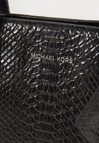 Sac à main noir avec une texture en cuir de serpent, présentant un logo "Michael Kors" en argent et des accents lisses. Le design est élégant et structuré.