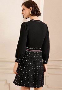 Abito nero con maniche a palloncino, scollatura a scalloped, vita a strisce e gonna plissettata con pois bianchi e dettagli rosa.