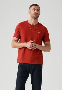 Tricou din bumbac roșu, cu gât rotund, mâneci scurte și un mic logo alb pe piept. Asortat cu blugi denim închis.