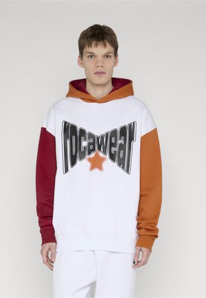 Nuori mies pukeutuneena valkoiseen huppariin, jossa on punaiset ja oranssit hihat ja suuri vääristynyt "rocawear"-logo ja tähti edessä.