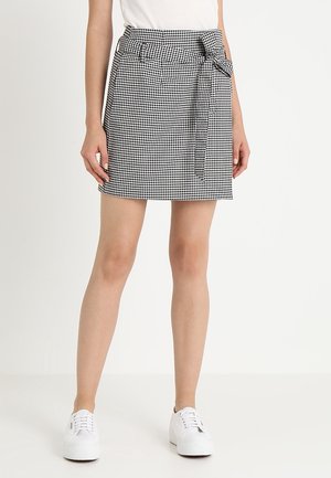 Mini falda de cuadro vichy en blanco y negro con lazo en la cintura, diseño estructurado y tela suave; combinada con zapatillas blancas para un look casual.