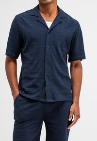 Marineblauwe short-sleeve shirt van textuurstof, met een knoopsluiting aan de voorkant en een open kraagontwerp. Gecombineerd met bijpassende broek.