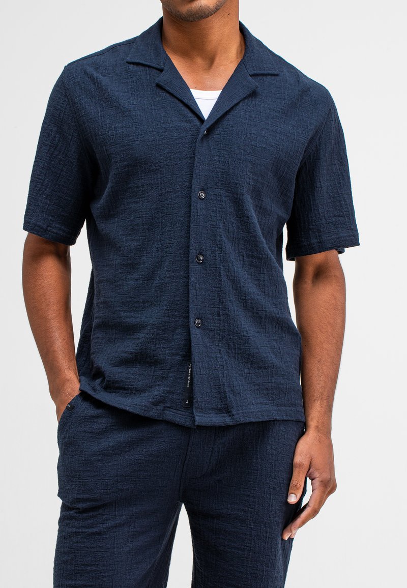 Marineblauwe short-sleeve shirt van textuurstof, met een knoopsluiting aan de voorkant en een open kraagontwerp. Gecombineerd met bijpassende broek.