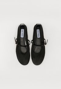 Chaussures en cuir noir avec un bout arrondi, une semelle plate et une bride au niveau de la cheville. Texture lisse avec un minimum de couture et un design simple et moderne.
