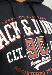 Navy hoodie featuring bold white and maroon text, with "Jack & Jones" prominently displayed, a classic pullover design, and drawstring.