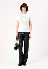 White t-shirt with a pastel geometric print, paired with black faux leather pants and platform shoes. Model holding a small black bag.