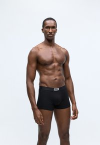 Black cotton boxer briefs with a wide waistband featuring a white "HUGO" logo. The fabric appears smooth and lightweight.