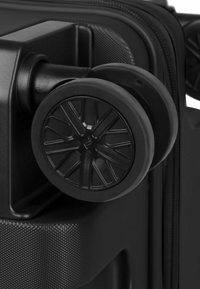 Angolo di una valigia rigida nera con superficie testurizzata, ruota nera robusta e asse in plastica rinforzata per una maggiore durata.