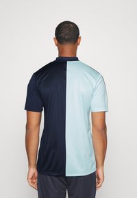 Polo de manga corta dividido en azul marino y azul claro, con cuello y tejido suave y ligero con un acabado ligeramente brillante.