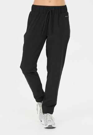 Zwarte joggerbroek met elastische taille en trekkoord, gedragen met witte sportschoenen, weergegeven op een staande persoon van taille tot voeten.