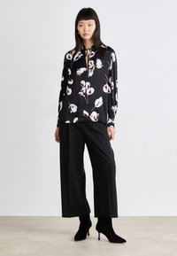 Svart blomstret bluse med hvite og rosa blomster, med V-hals og knytedetalj. Kombinert med løse svarte bukser og svarte hælboots.