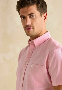 Košeľa s krátkym rukávom, s golierom, v pevnej ružovej tkanine s textúrovaným povrchom, so sieťovanou vreckom na hrudi a malým vyšitým logom.