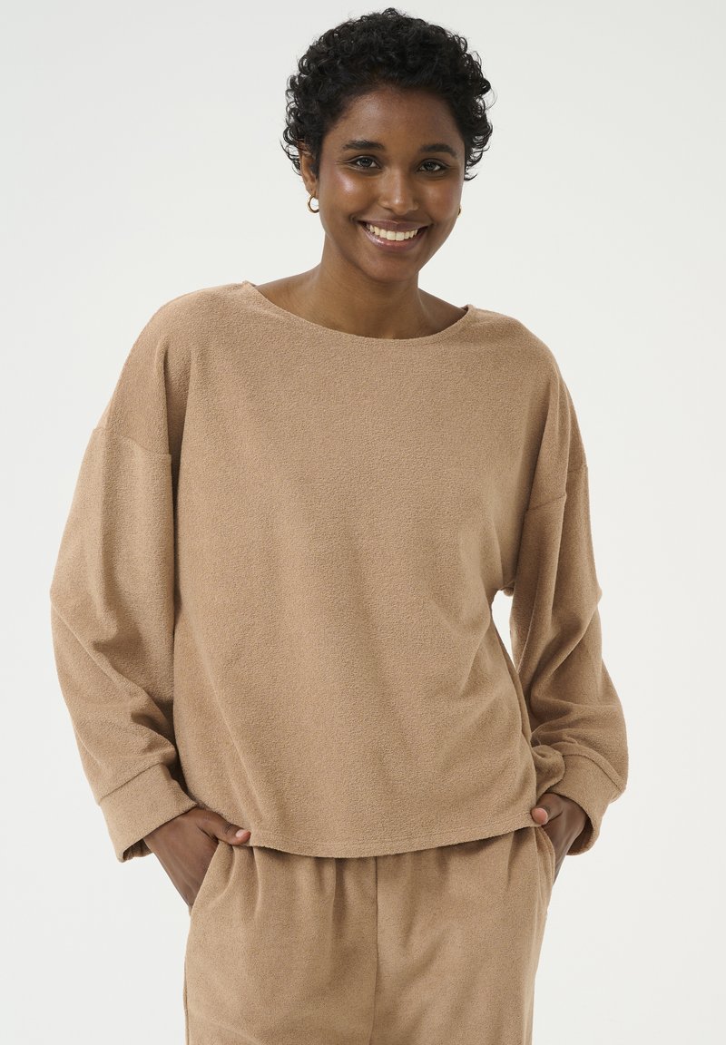 Beiger oversized Pullover mit rundem Ausschnitt und langen Ärmeln, aus weichem, strukturiertem Stoff gefertigt, stilvoll kombiniert mit locker sitzenden passenden Hosen.
