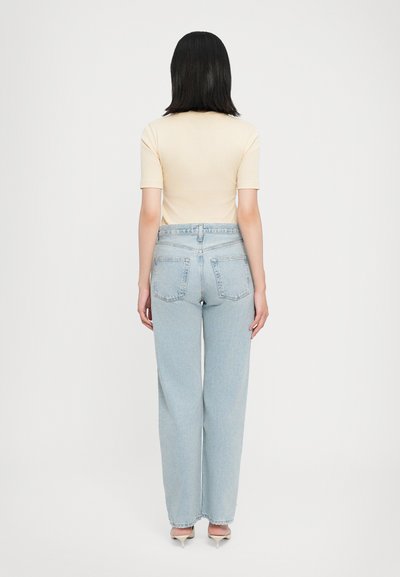 Light beige fitted top paired with high-waisted, loose-fit light blue denim jeans featuring back pockets and a clean hem.