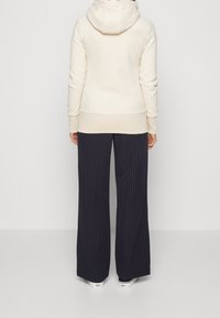 Sudadera beige con capucha, con dobladillos y puños acanalados, combinada con pantalones de pierna ancha a rayas navy, llevada con zapatos blancos.