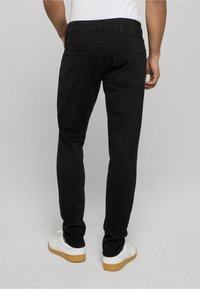 Melni pieguļoši džinsi ar gludu tekstūru, kuriem ir divas aizmugurējās kabatas un redzamais jostas uzraksts. Papildināti ar baltām sporta kurpēm ar gumijas zoli.