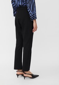 Zwarte tapers met een gladde textuur, voorzien van een hoge tailleband. Gecombineerd met zwarte slingback schoenen met een puntige neus en een lage hak.